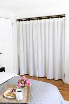 a tray with food on top of a bed next to a white wall and window