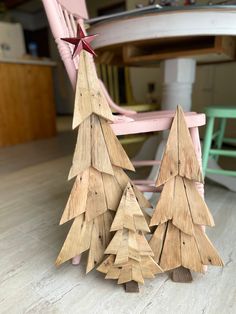 two wooden christmas trees sitting on top of a hard wood floor next to a pink chair