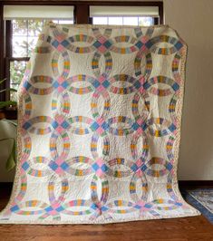 a white quilt with multicolored circles is on the floor next to a potted plant