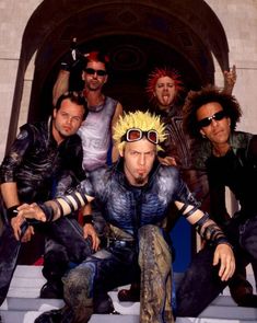 a group of men with weird hair and sunglasses posing for a photo in front of a building