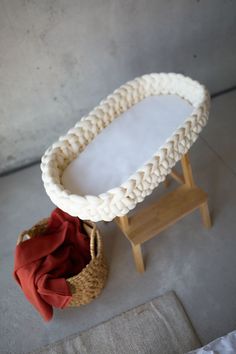 a white crocheted baby bassinet next to a red blanket and wooden stool