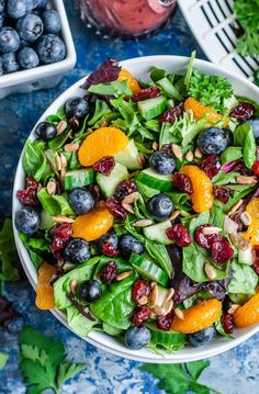 a salad with oranges, blueberries and almonds in a white bowl on a blue table