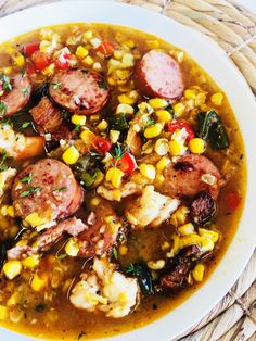 a white bowl filled with corn and sausage soup on top of a wicker place mat