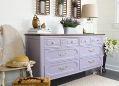 a purple dresser in a white room with flowers on the top and two mirrors above it