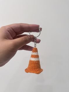 a hand holding an orange and white crochet bell keychain