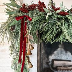 a christmas wreath with bells and greenery hanging from it's side, next to a fireplace