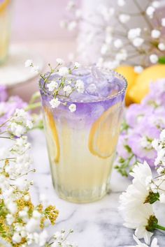 a glass filled with lemonade sitting on top of a table next to white flowers