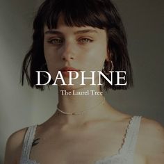 a woman with dark hair wearing a white top and necklace, standing in front of the words dappne