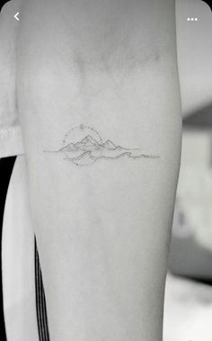 a person with a small mountain tattoo on their left arm and the outline of a mountain behind them