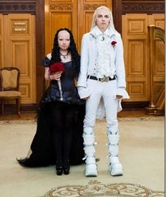 two women dressed in white and black standing next to each other on the floor with wooden doors behind them