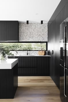 a kitchen with black cabinets and white counter tops, along with a window that looks out onto the trees outside