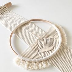 a white wall hanging with tassels on it and a wooden hoop in the middle