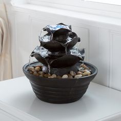 a black potted plant with rocks and water running down it's side in front of a window