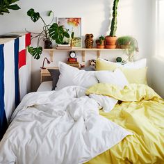 a bed with yellow sheets and pillows in a bedroom next to a potted plant