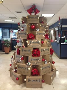 a christmas tree made out of boxes with red bows and ornaments on it in an office lobby