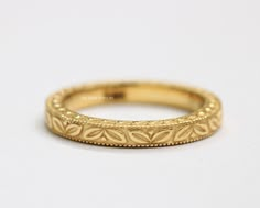 a gold wedding band that has been engraved with leaves on the inside and outside, sitting on a white surface