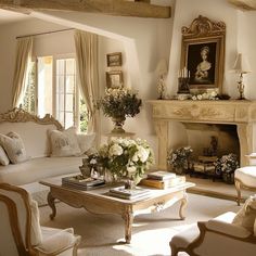 a living room filled with white furniture and flowers on top of a coffee table in front of a fire place