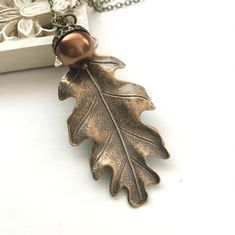 "Here is a fabulous oak leaf necklace featuring a large brass oak leaf which is nicely detailed, along with one acorn which hangs in front of the leaf. The acorn consists of a copper colored glass pearl and a textured brass acorn bead cap. This necklace comes on a nice quality soldered brass chain and is closed with a solid brass clasp. Comes packaged in a sweet Botanical Bird gift box. You may also choose a different colored acorn from the drop down menu, choose from copper (as pictured), green Oak Leaf Necklace, Gold Leaf Necklace, Woodland Jewelry, Acorn Necklace, Autumn Necklace, Best Friend Necklaces, Copper Glass, Friendship Jewelry, Long Beaded Necklace