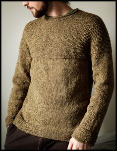 a man wearing a brown sweater standing in front of a white wall