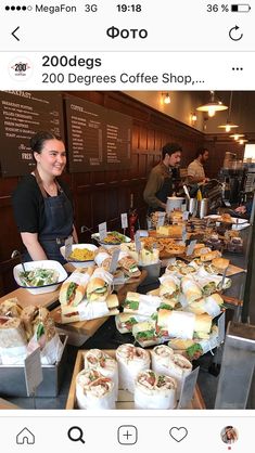 a woman standing in front of a counter filled with sandwiches and other food on trays