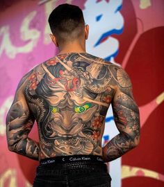 the back of a man with tattoos on his body and chest, standing in front of a colorful wall