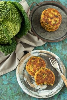 two crab cakes on plates with a fork and head of cabbage in the background,