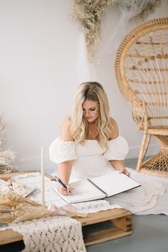 a woman sitting at a table with a notebook and pen in front of her, surrounded by wicker chairs