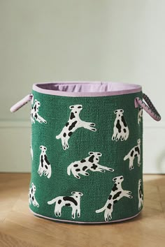 a green and white dog print fabric storage bin with purple lining on the bottom, sitting on a wooden floor