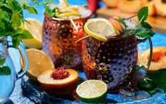 two glasses filled with liquid and garnished with lemons, limes and mint