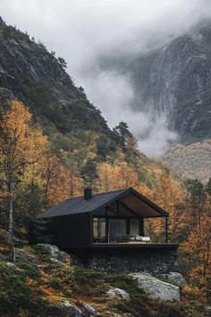 a cabin in the mountains surrounded by trees with yellow leaves on it's branches