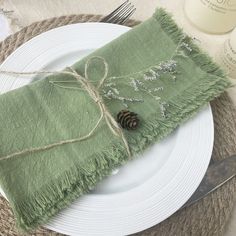 a place setting with green napkins, silverware and a pine cone on top