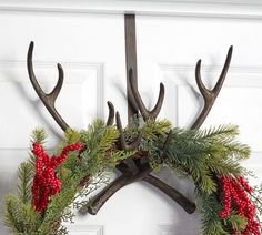 two antlers with red berries and green leaves on them hang from a metal hook in front of a white door