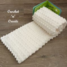 a white crochet scarf sitting on top of a wooden floor next to a box