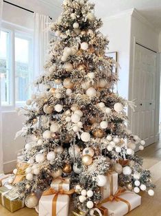 a white christmas tree with gold and silver ornaments on it, wrapped presents under the tree