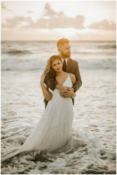 a bride and groom standing in the surf at sunset on their wedding day, embracing each other