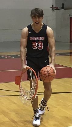 a young man holding a basketball on top of a basketball court with a hoop in his hand