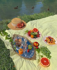 a picnic with fruit, watermelon and other foods on a blanket by the river