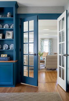 a blue bookcase with plates on it in front of an open door to the living room