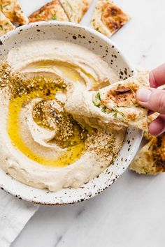 a person dipping hummus into a white bowl