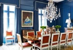 an elegant dining room with blue walls and chandelier hanging from the ceiling, along with red upholstered chairs