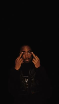 a man is holding his hands up to his face in front of the dark background