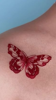 a red butterfly tattoo on the back of a woman's shoulder and chest area