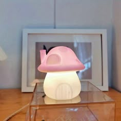 a pink mushroom lamp sitting on top of a glass table next to a framed photo