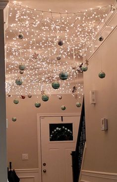 christmas lights hang from the ceiling above a white door and staircase leading up to an entryway