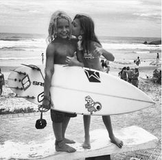 two girls are standing on the beach with their surfboards and holding onto each other