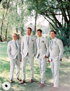 a group of men standing next to each other wearing suits and ties on grass covered ground