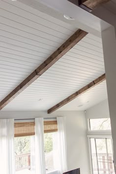 a living room with white walls and wooden beams on the ceiling, along with large windows