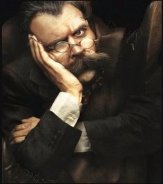 a man with glasses and a beard is sitting in a chair looking at the camera