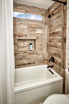 a white toilet sitting next to a bath tub under a window in a bathroom with wooden walls