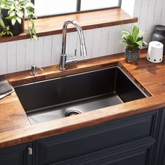 a kitchen sink sitting under a window next to a counter top with potted plants